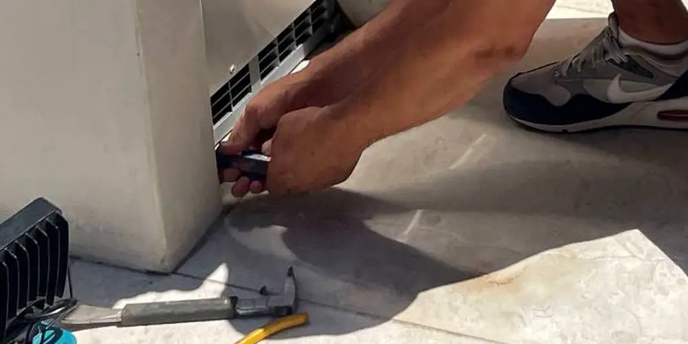 Close on Danny's hands driving a screwdriver, with a work light, hammer and pliers laid out on the concrete