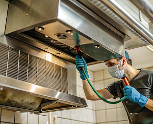 Technician cleaning a commercial kitchen exhaust hood