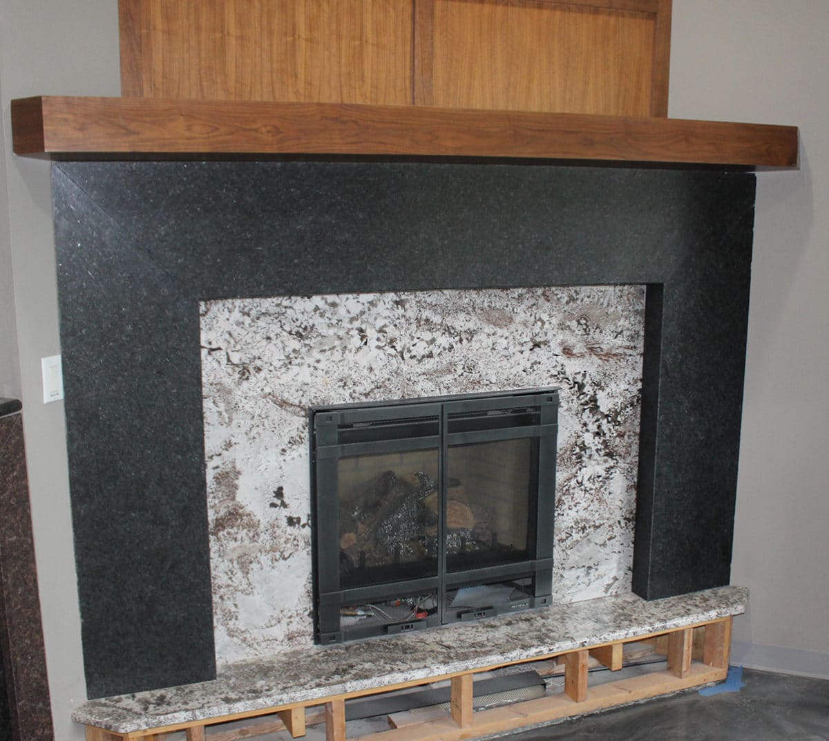 Black granite fireplace surround with white natural stone panel and wood mantel