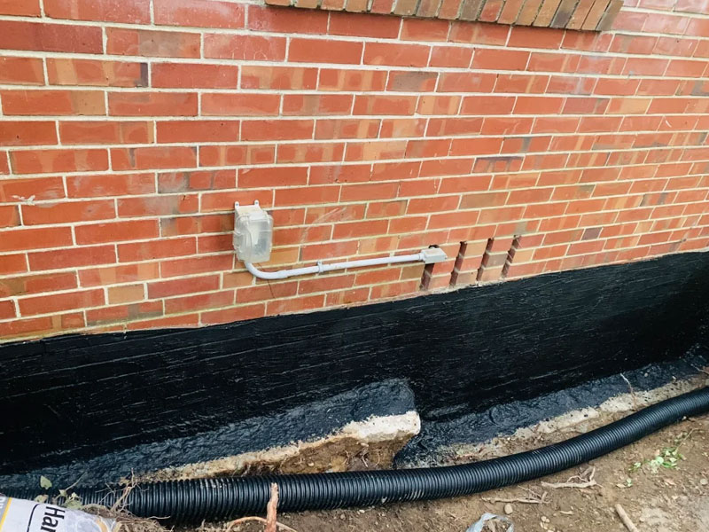Waterproof membrane and drainage installed against a brick foundation in an open trench