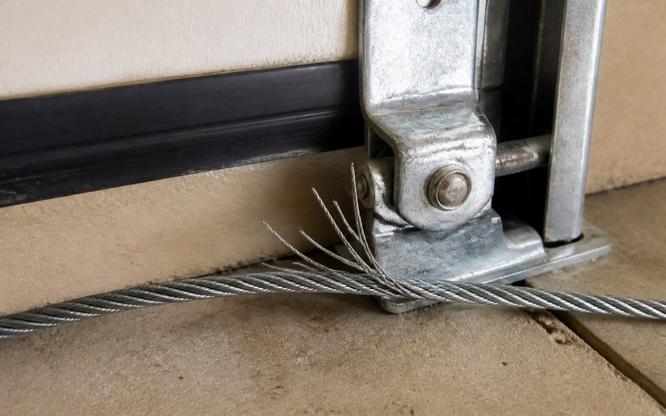 Frayed garage door lift cable with broken steel strands at the bottom bracket