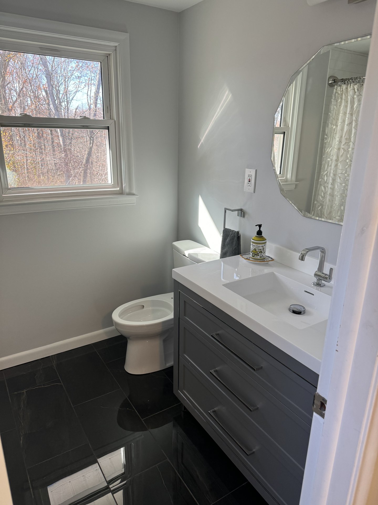 Renovated bathroom with a grey vanity, quartz top and dark marble-look floor tile