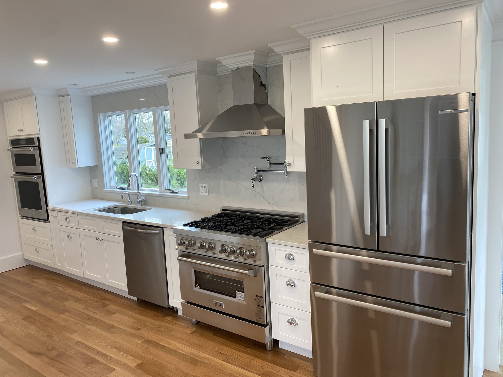 Renovated white shaker kitchen with a marble slab backsplash, pot filler and professional range