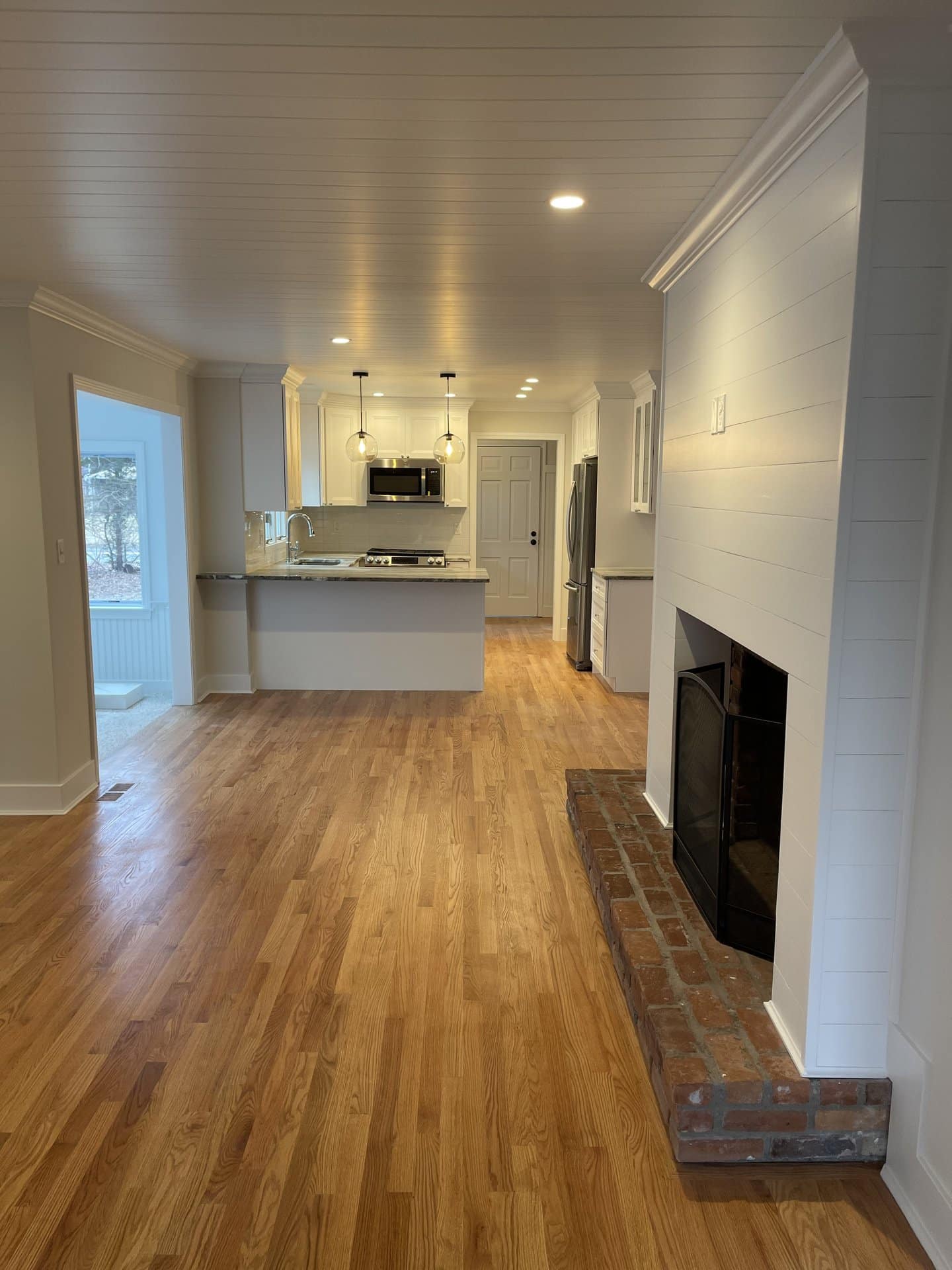 Open-plan kitchen and living space with a shiplap fireplace surround and red oak floors