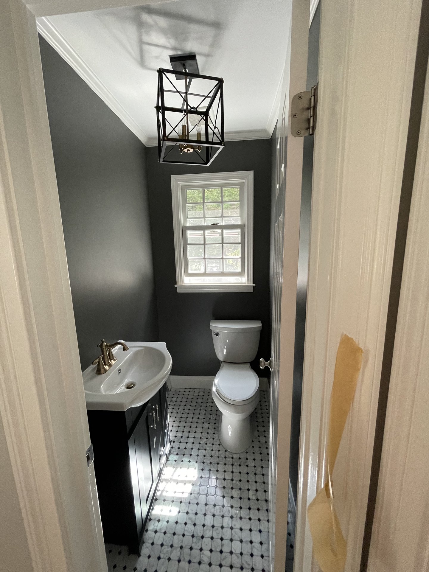 Renovated powder room with marble octagon-and-dot floor tile, dark walls and a lantern light
